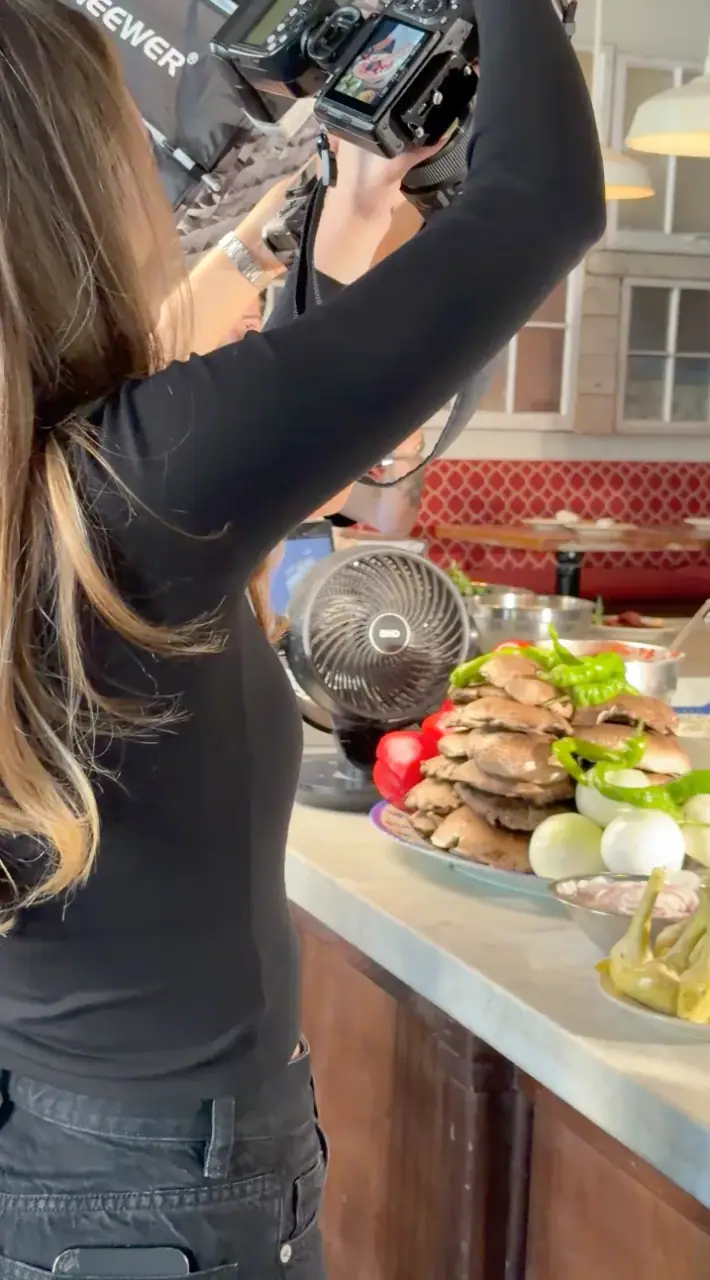 Behind the scenes at a DC Pie Co. shoot — a photographer frames a spread of sandwiches and toppings overhead with a rigged camera and LED light.