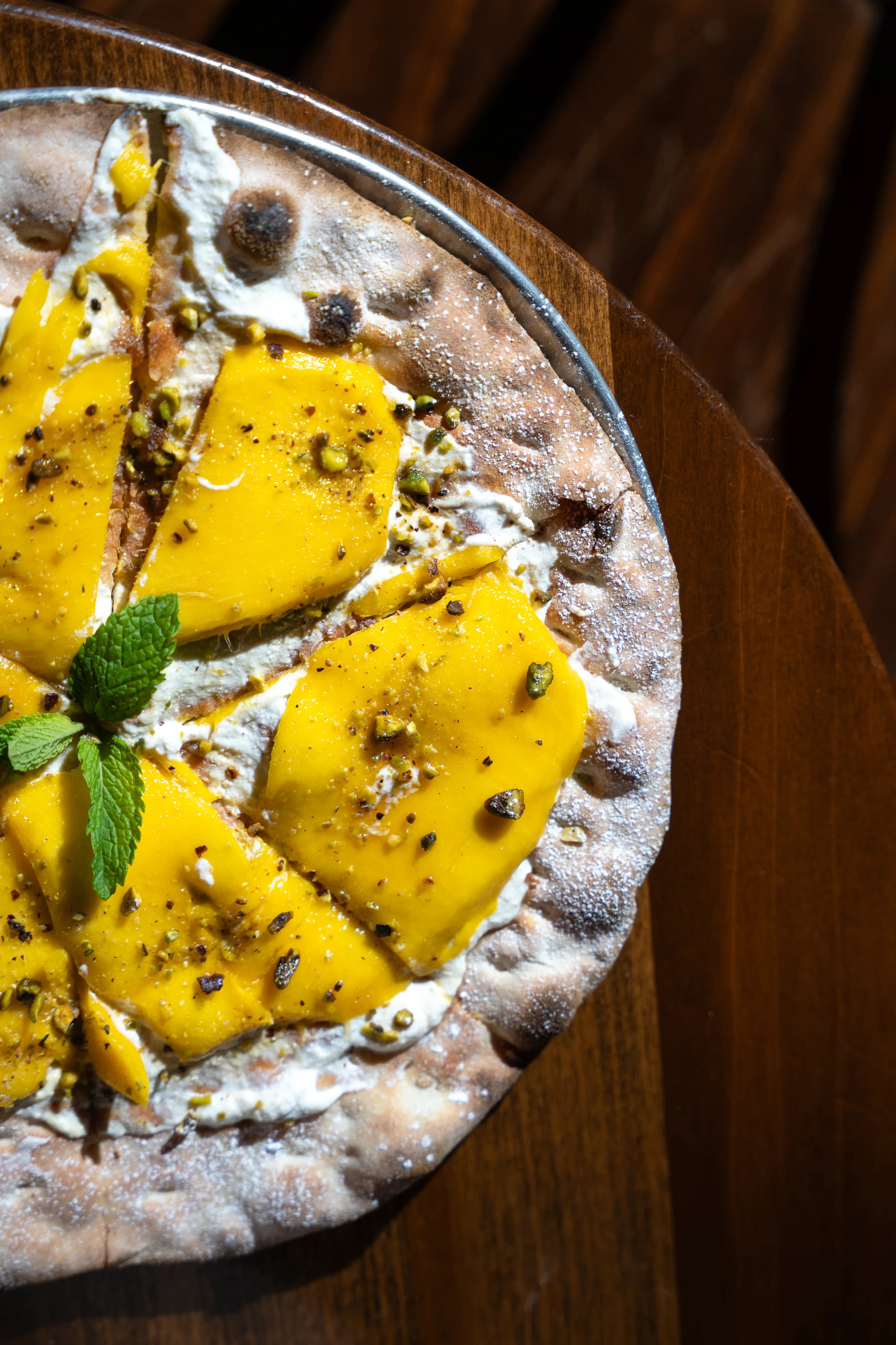 Overhead of a mango-and-cheese flatbread topped with mint and pistachio on a wood board at DC Pie Co.