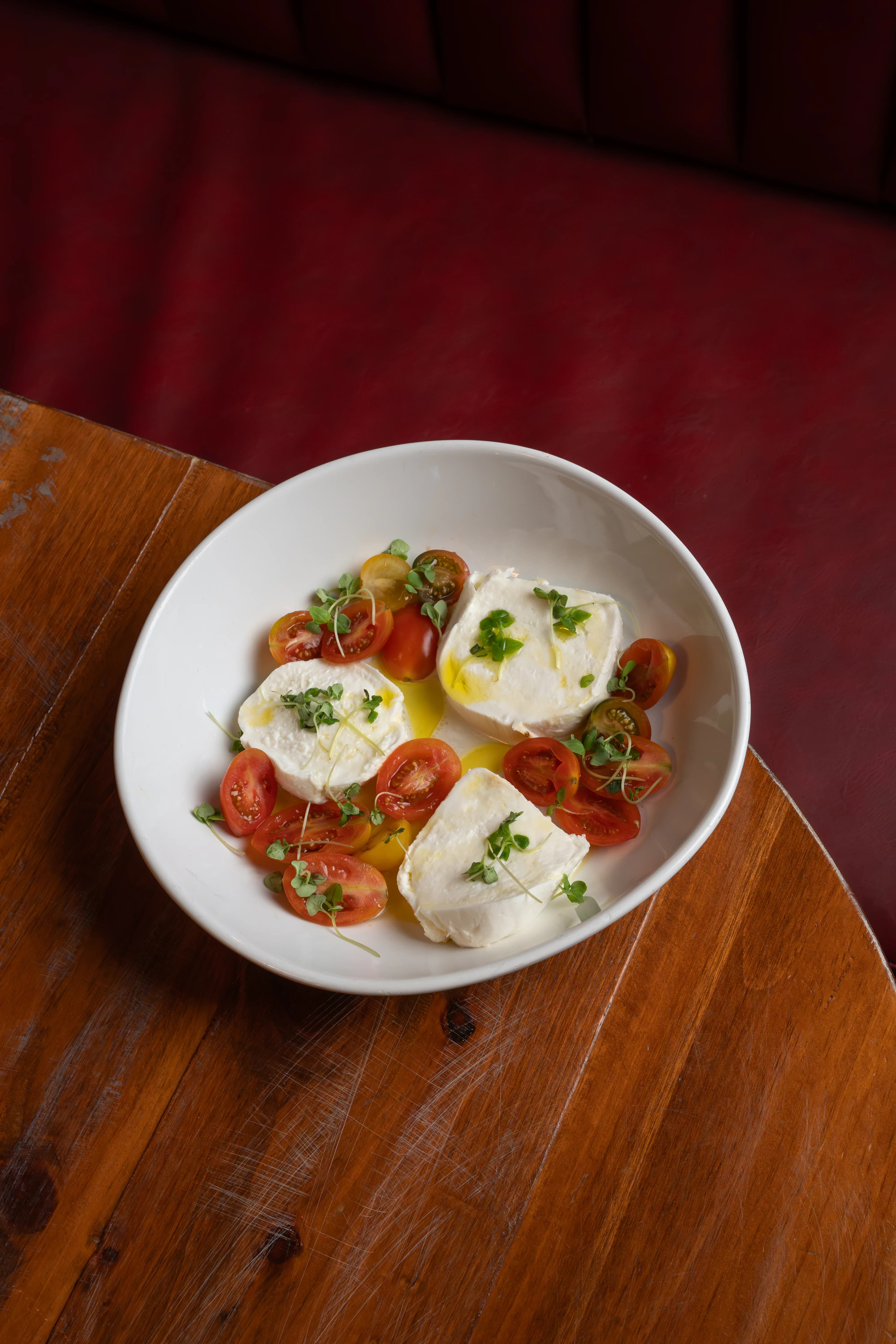 Burrata with blistered tomatoes and herbs in a white bowl on a wood table at DC Pie Co.