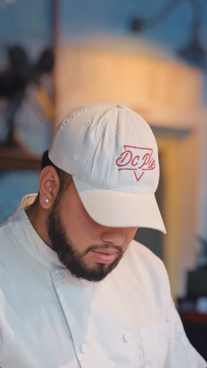 A DC Pie Co. team member in chef's whites and a pink-logo 'DC Pie' cap.