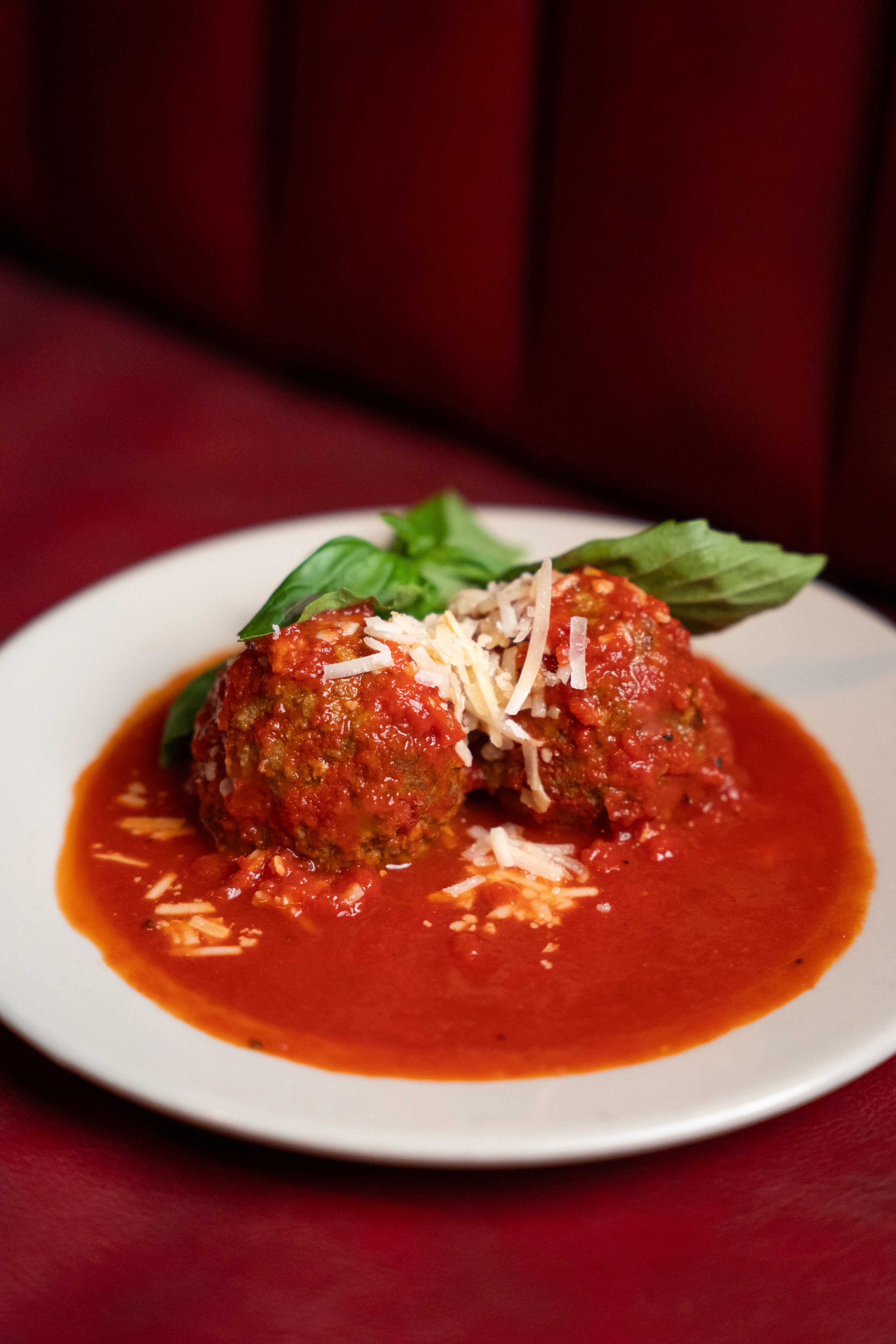 Two meatballs in tomato sauce topped with basil and parmesan on a white plate against red velvet at DC Pie Co.