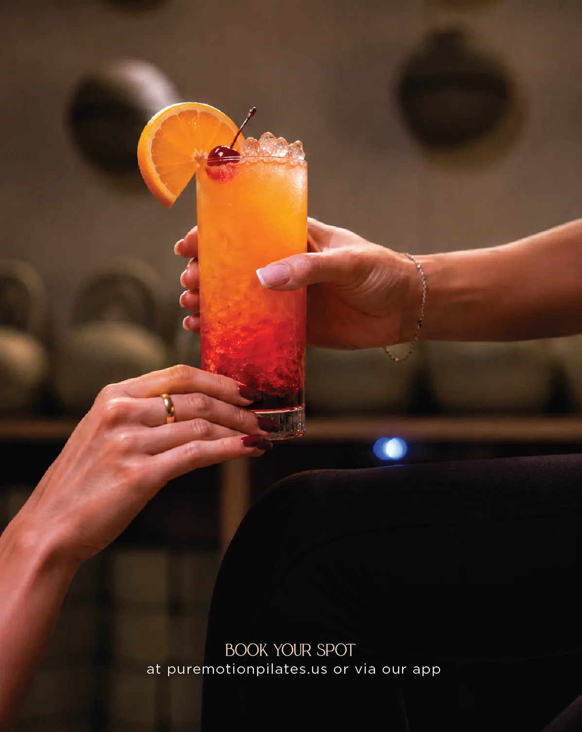 A Pure Motion promo — a hand holds a citrus cocktail over a reformer with a booking call-to-action.
