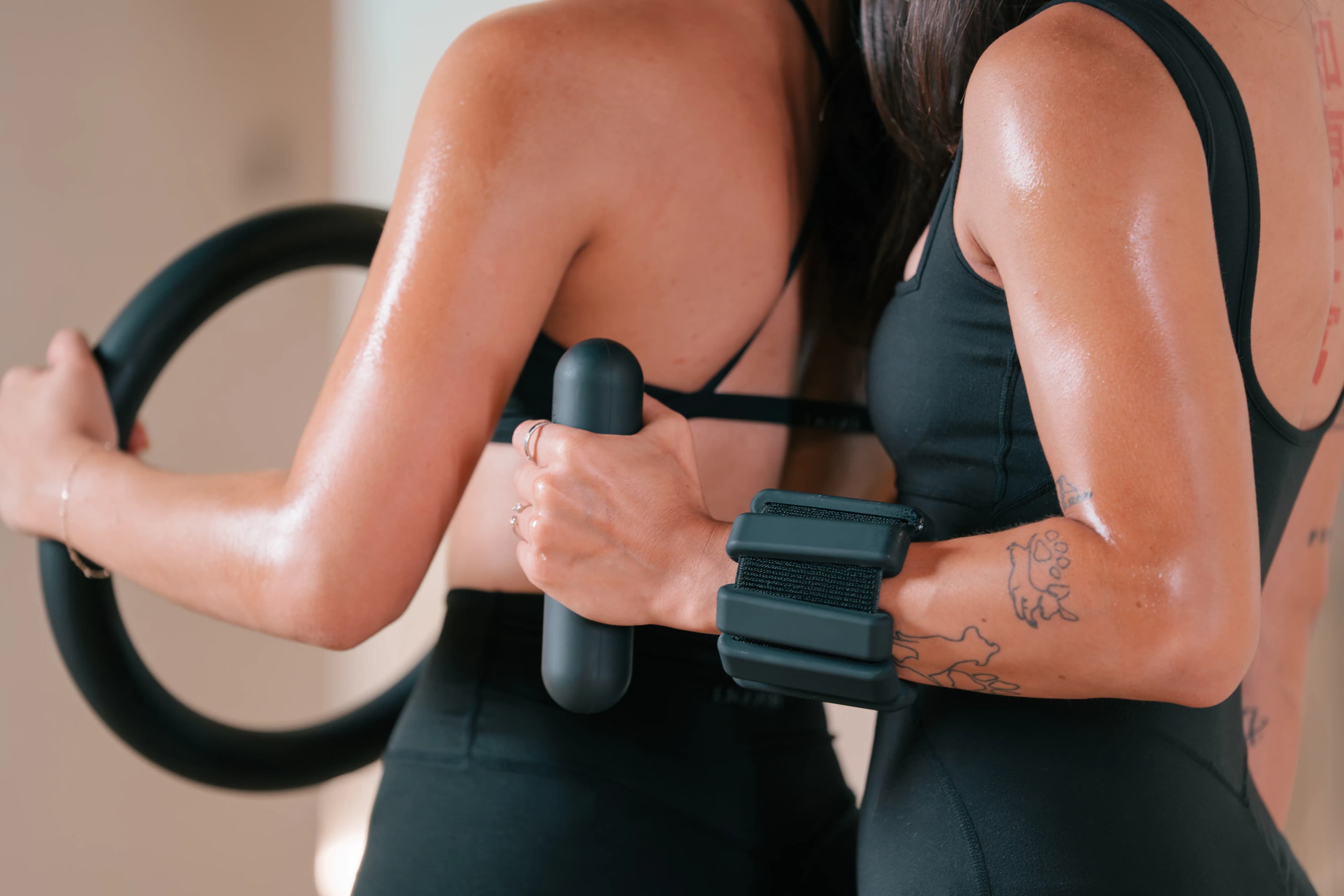 Two women in black activewear press a pilates ring between them in a bright studio at Pure Motion.