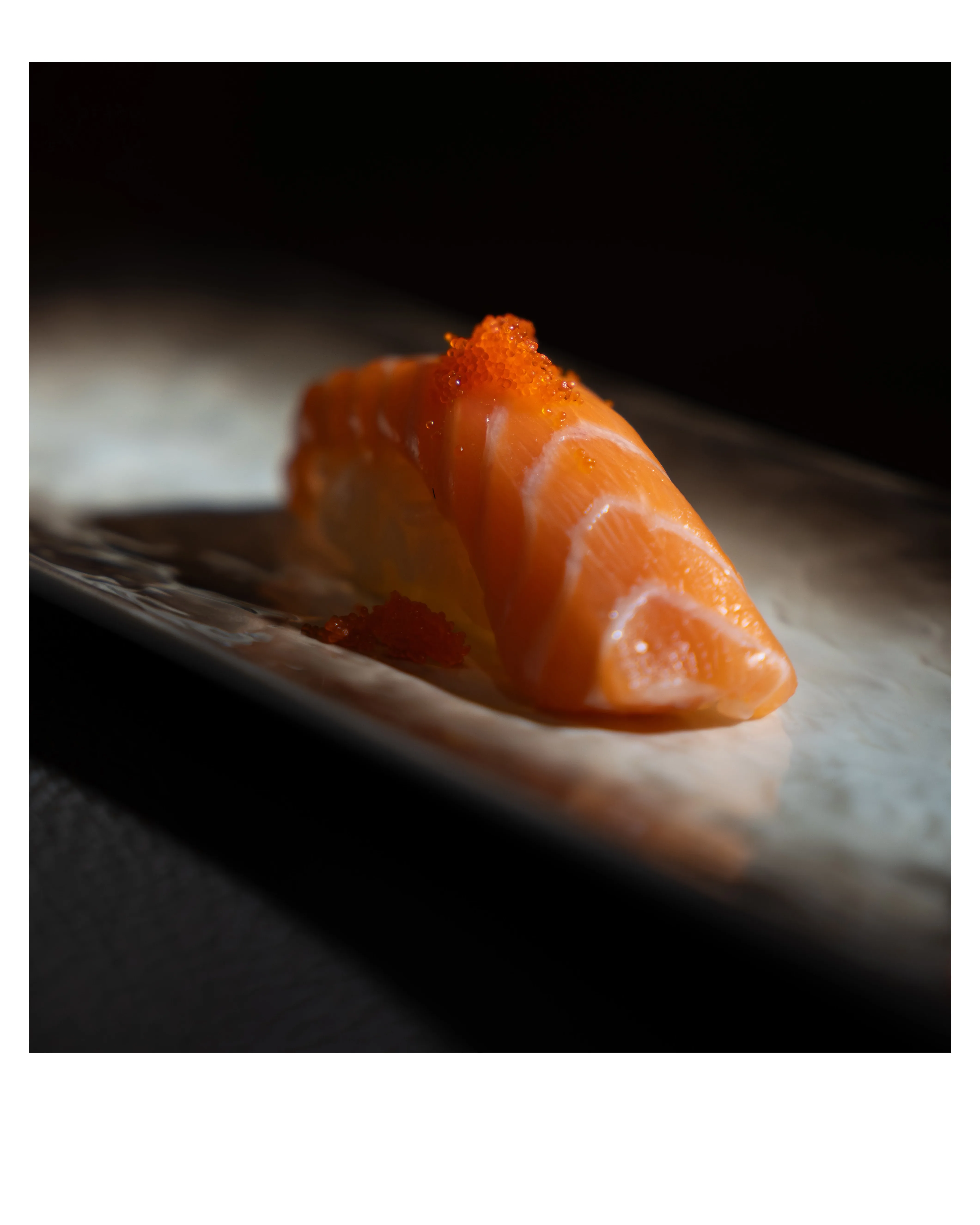 A piece of salmon nigiri topped with tobiko, spotlit on a ceramic plate at Sushi Sake.