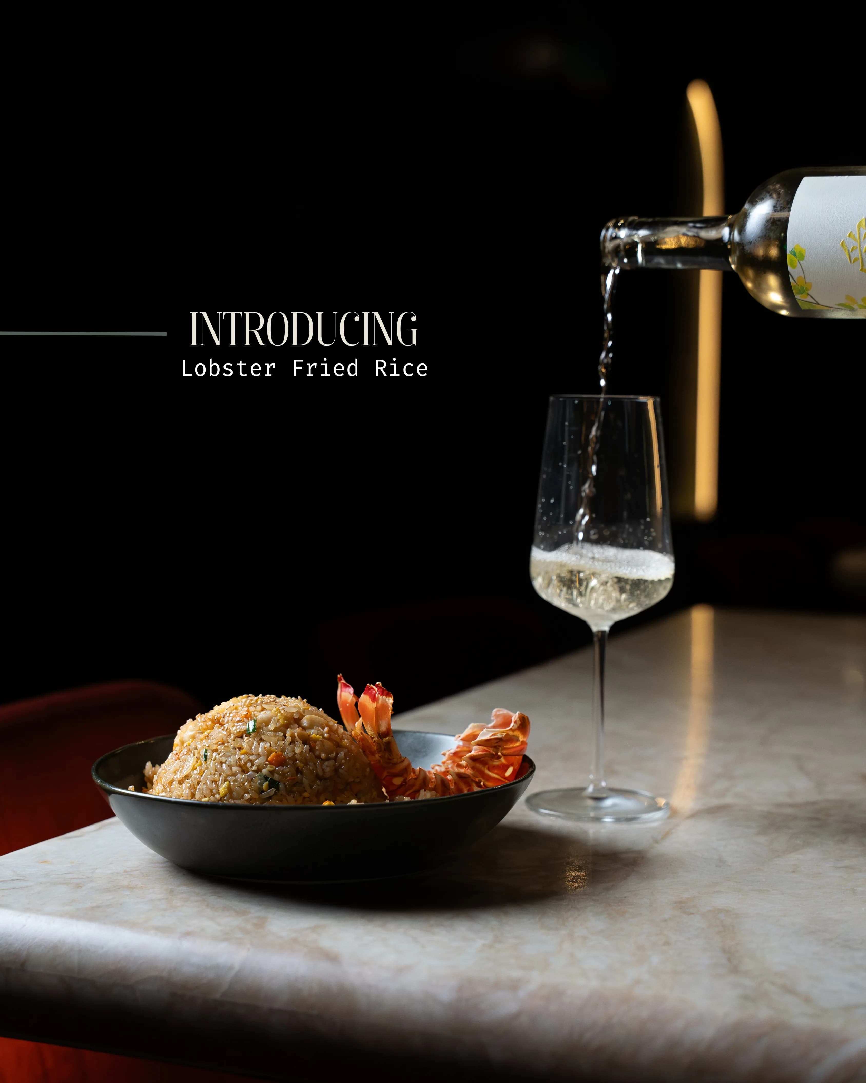 A Sushi Sake 'Introducing Lobster Fried Rice' promo graphic — the plated dish beside a glass of white wine being poured, set in moody light.