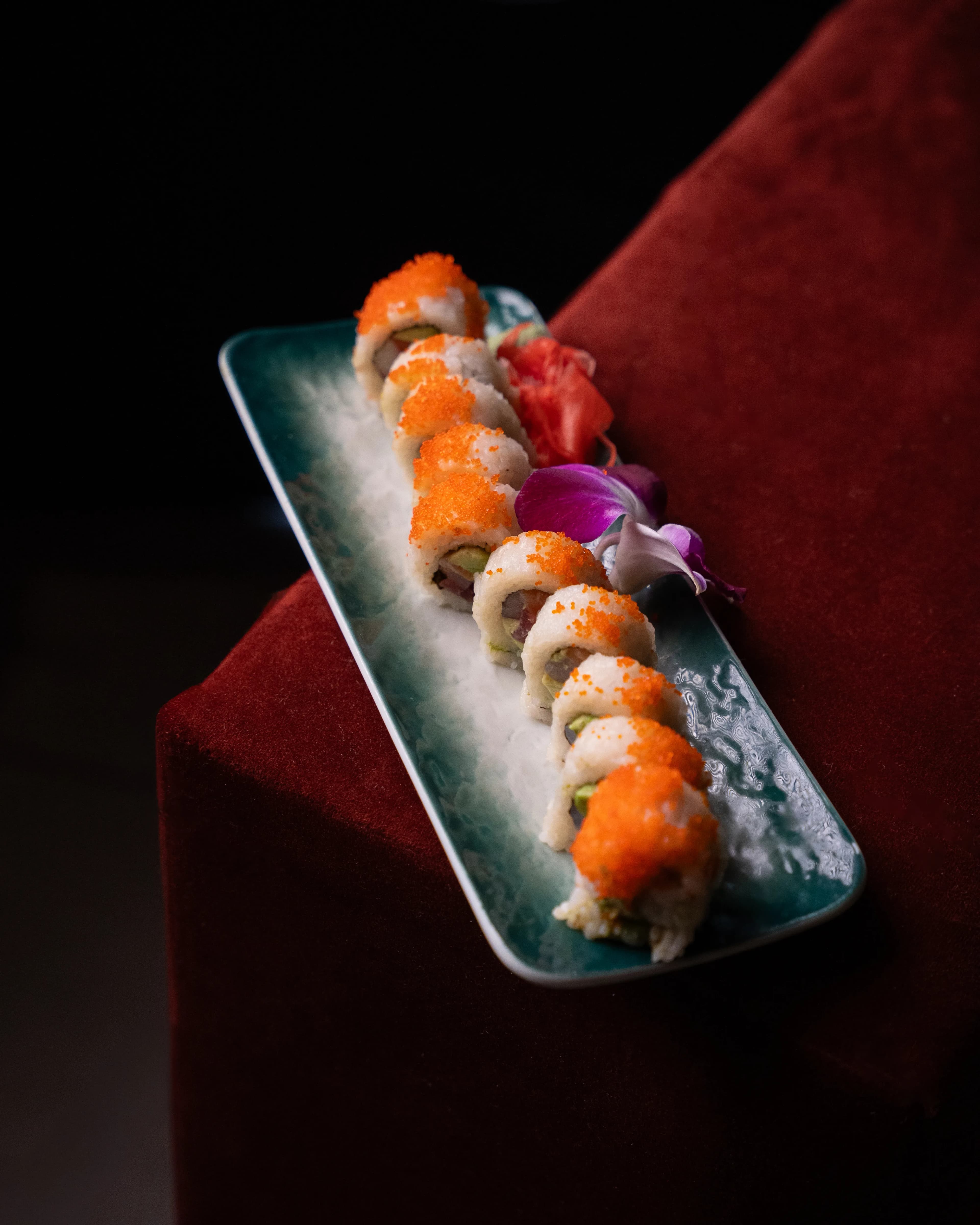 A long specialty sushi roll plated on a dark dish against red velvet at Sushi Sake.