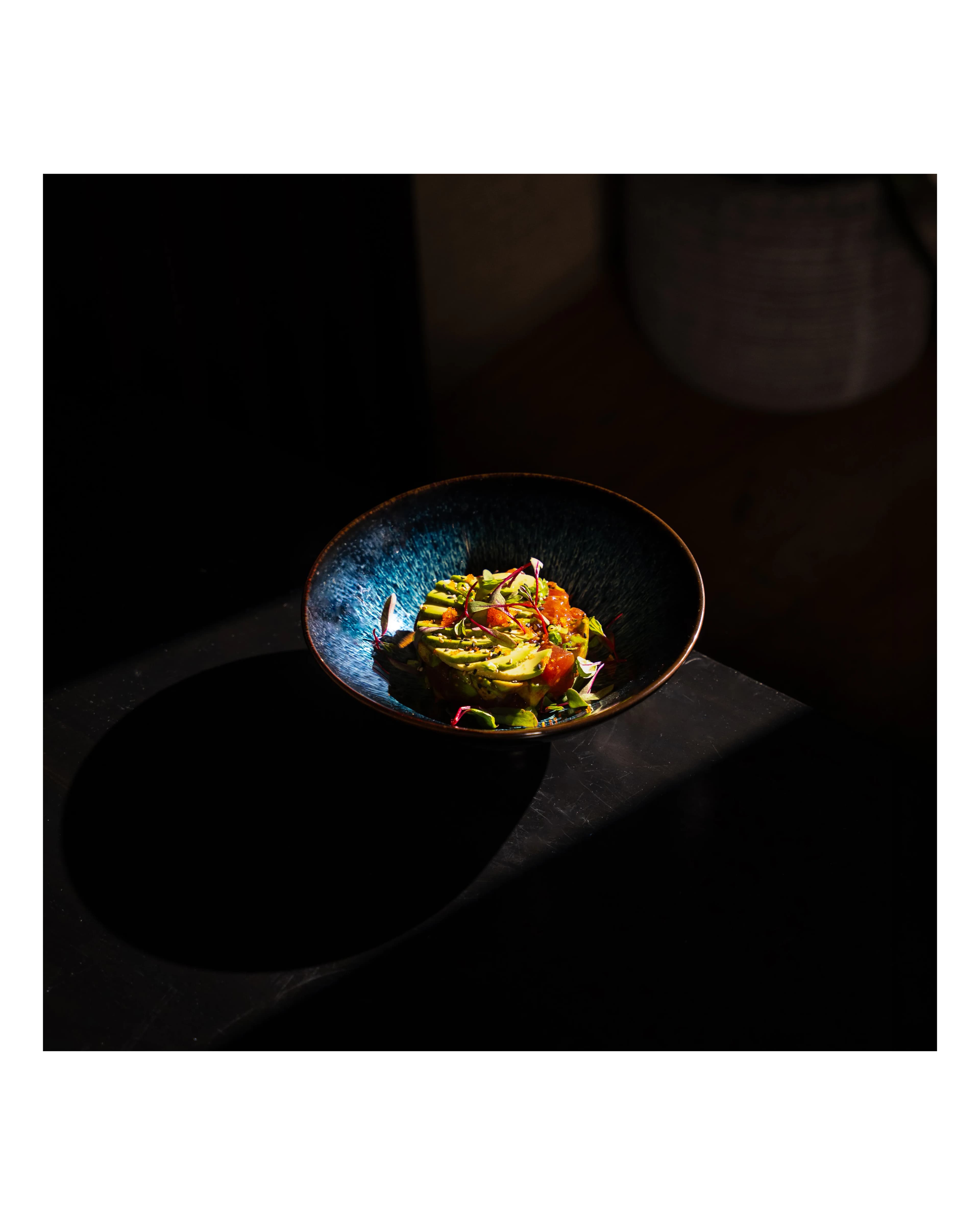 A spotlit bowl of plated food glows against a dark table at Sushi Sake.