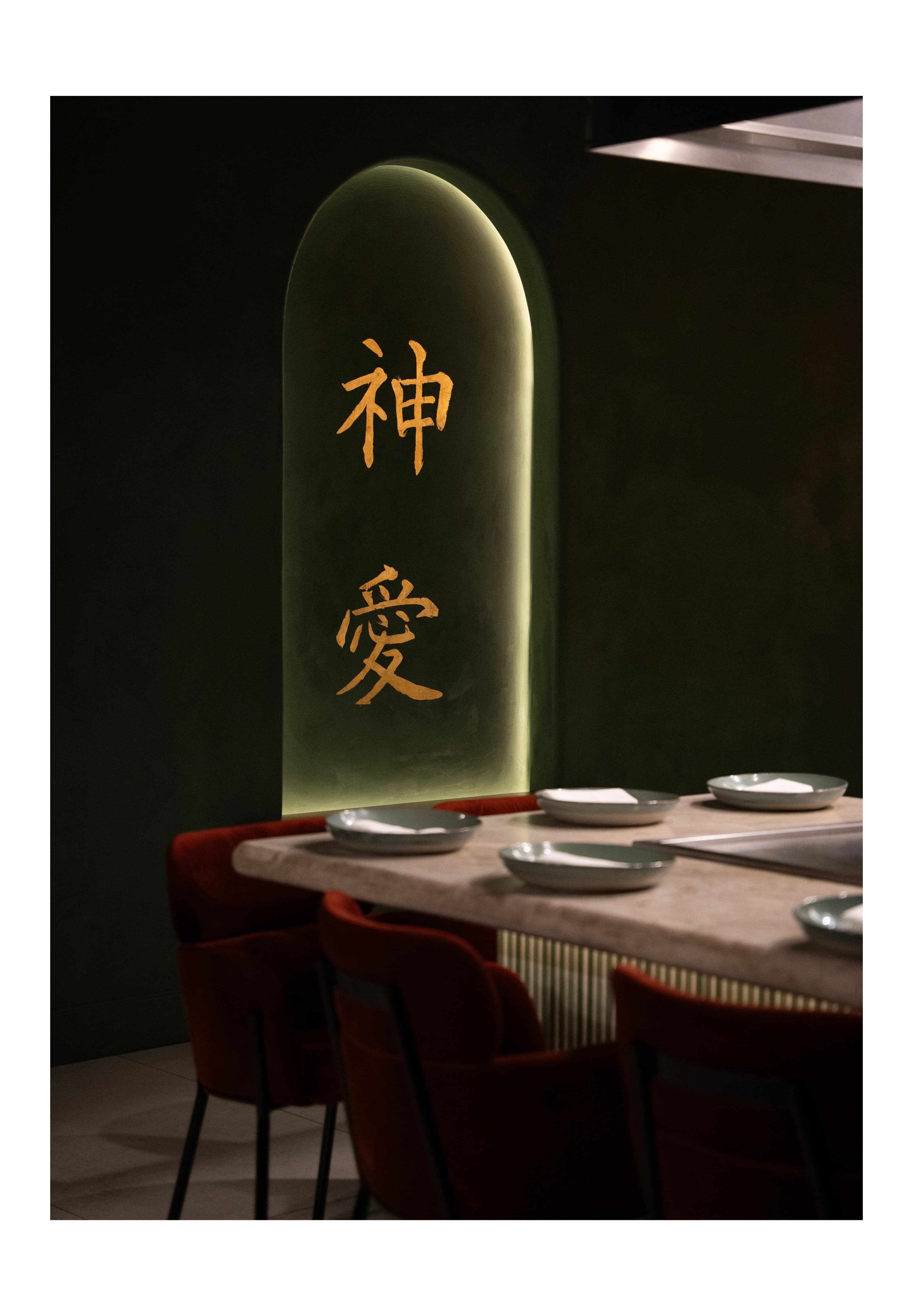 A glowing arched niche lettered with Japanese kanji above a set table with red chairs at Sushi Sake.