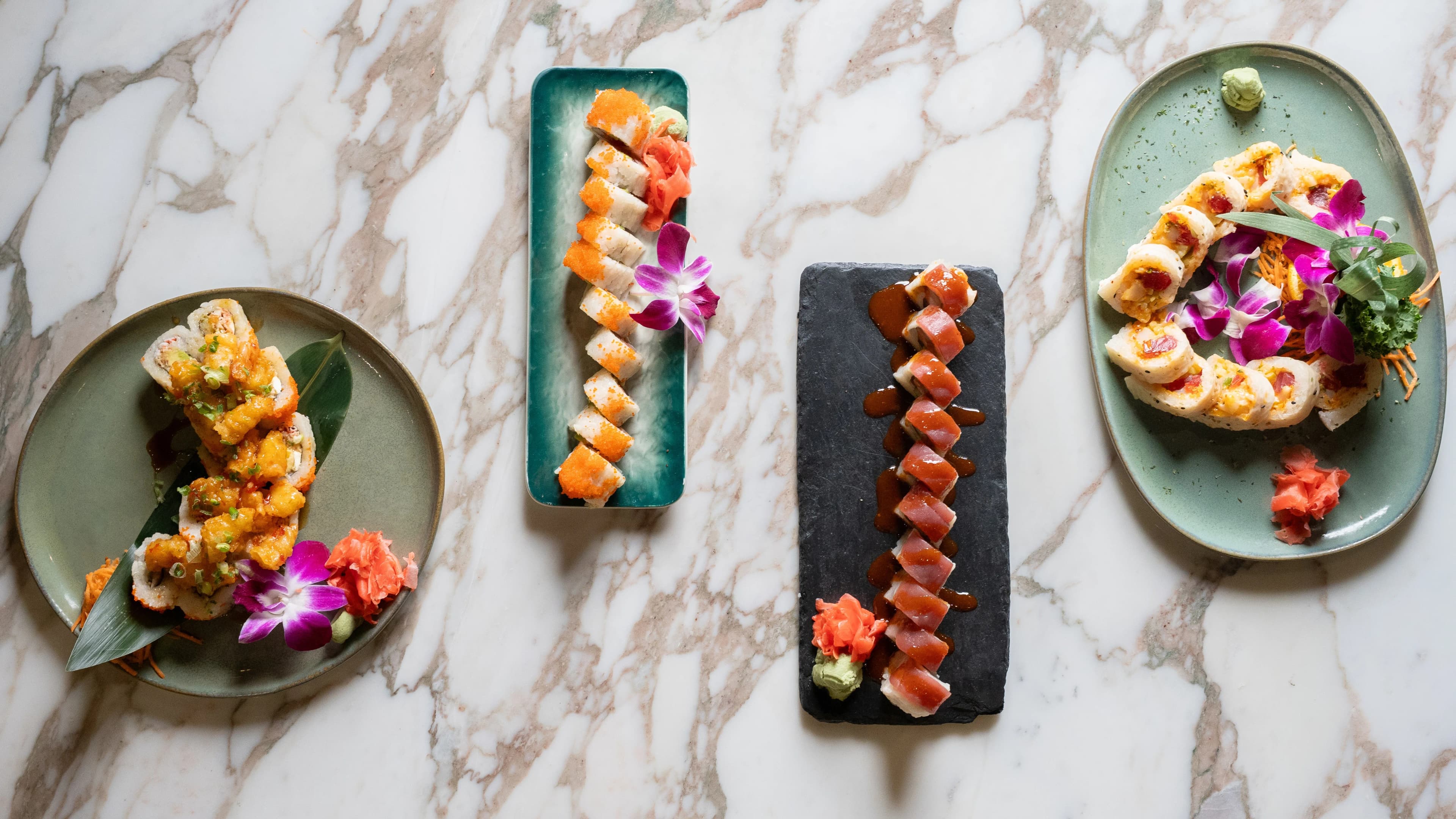 An overhead of three plated Sushi Sake rolls on marble.