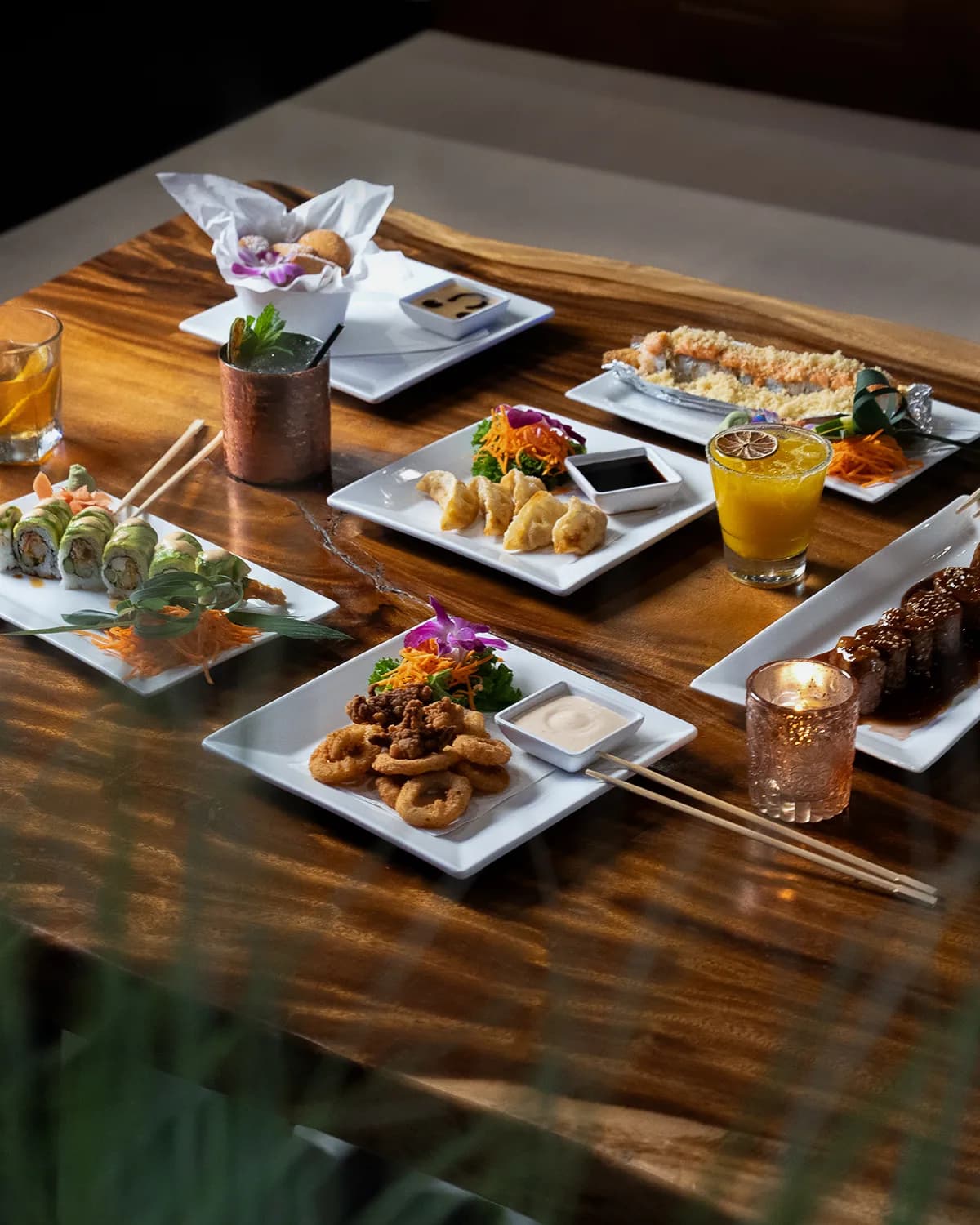 A styled table of Sushi Sake dishes and cocktails in warm light.