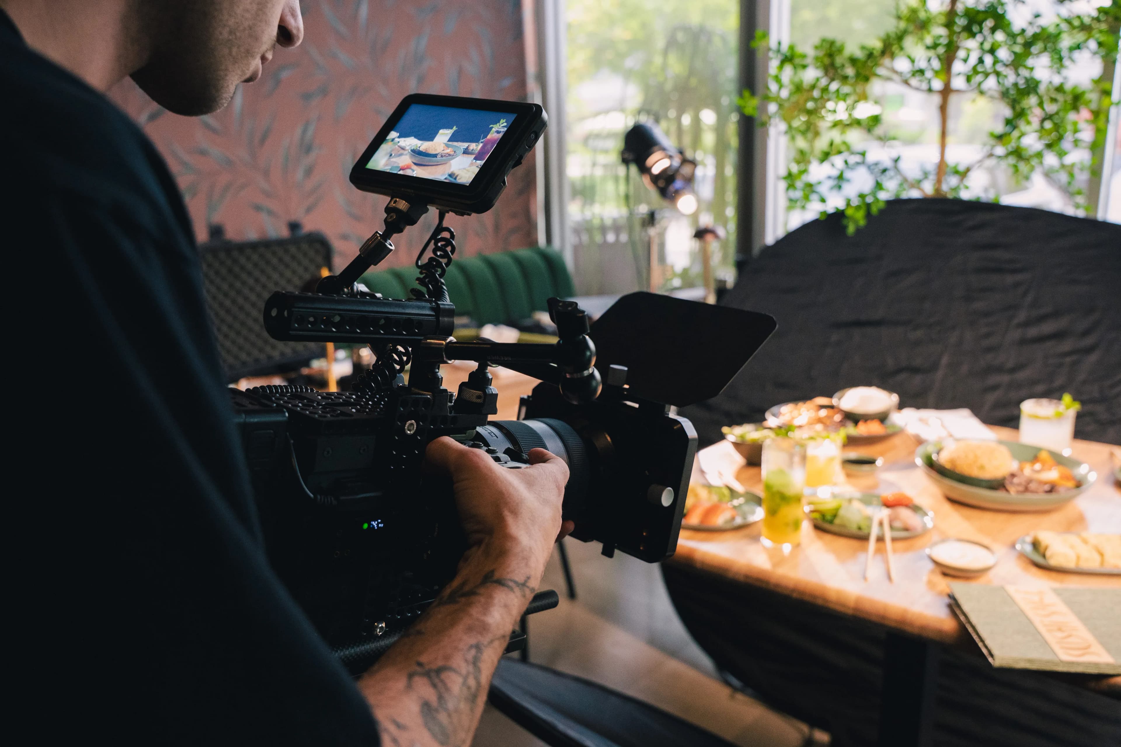 Behind the scenes — a camera operator films a Sushi Sake food setup by a window.