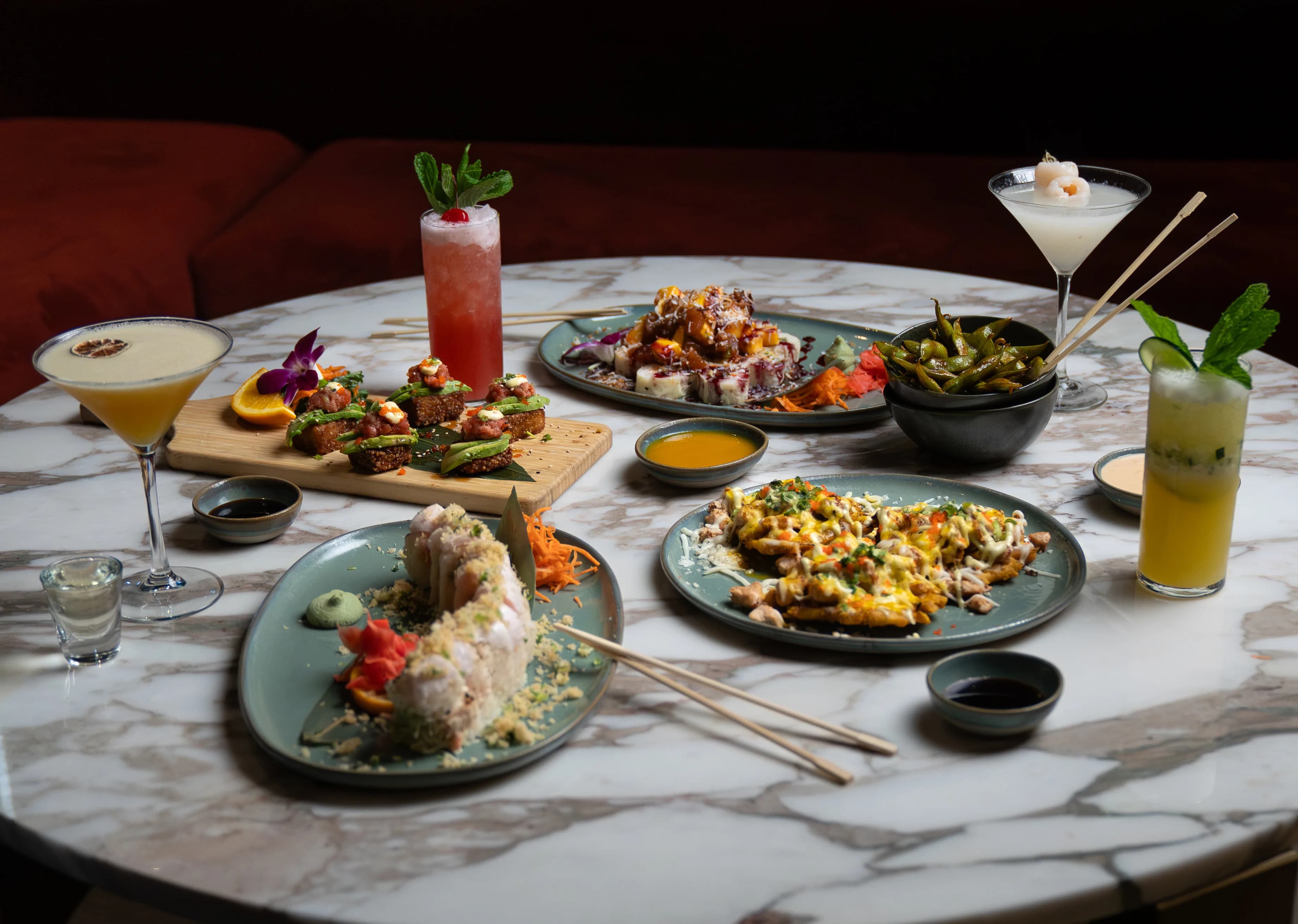 A round marble table of Sushi Sake dishes and cocktails against a red booth.