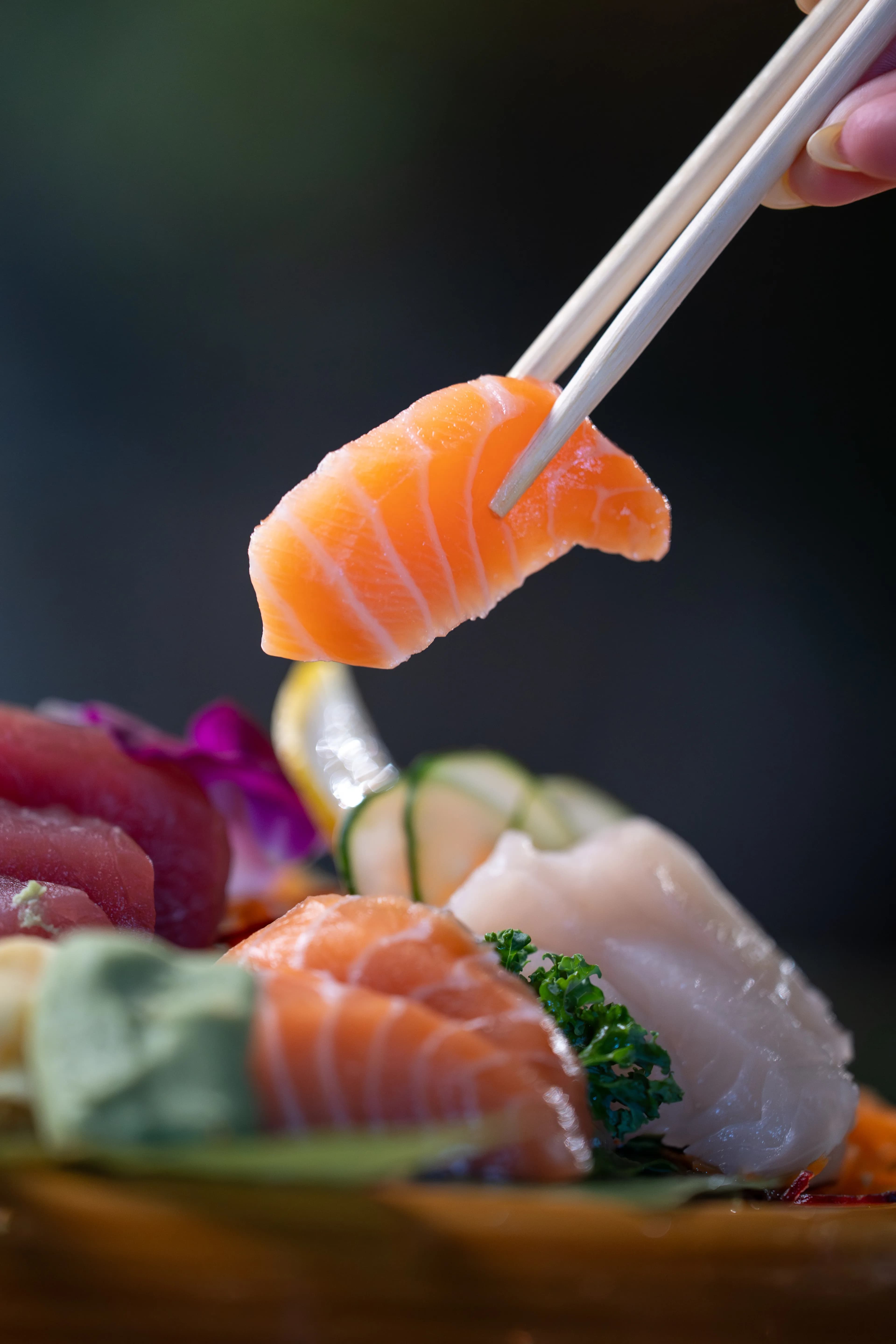 Chopsticks lift a piece of salmon over a Sushi Sake sashimi plate.